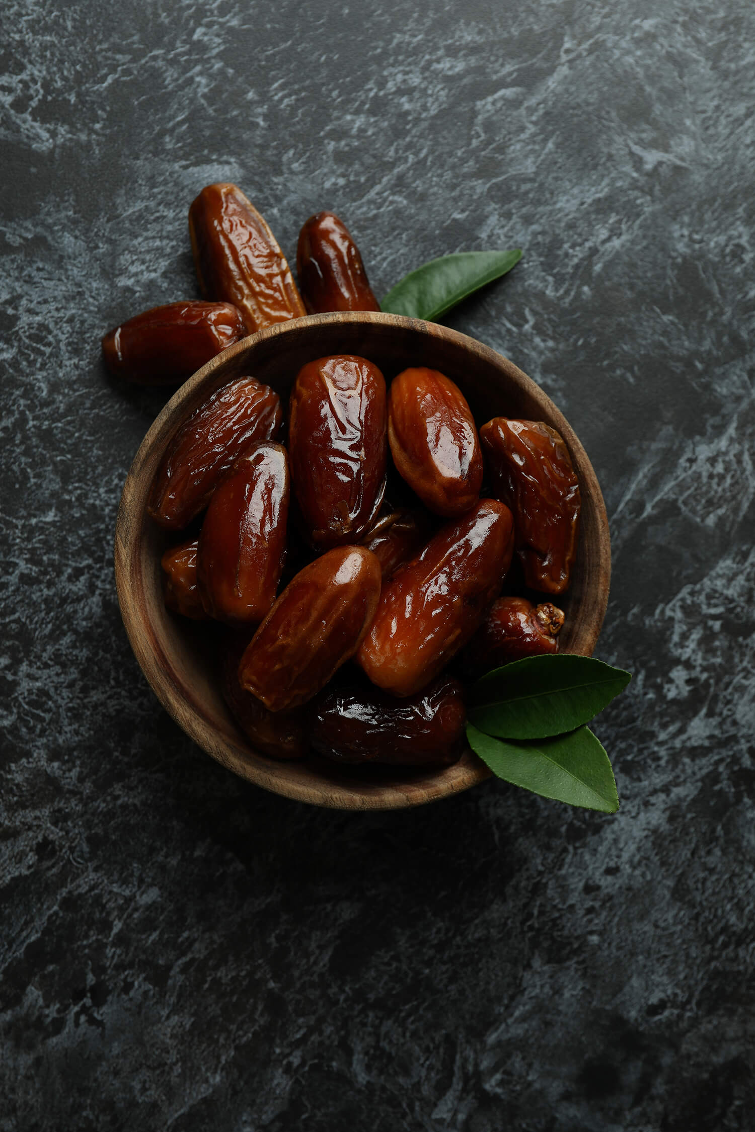 wooden-bowl-of-dates-on-black-smokey-background-FMXK96U